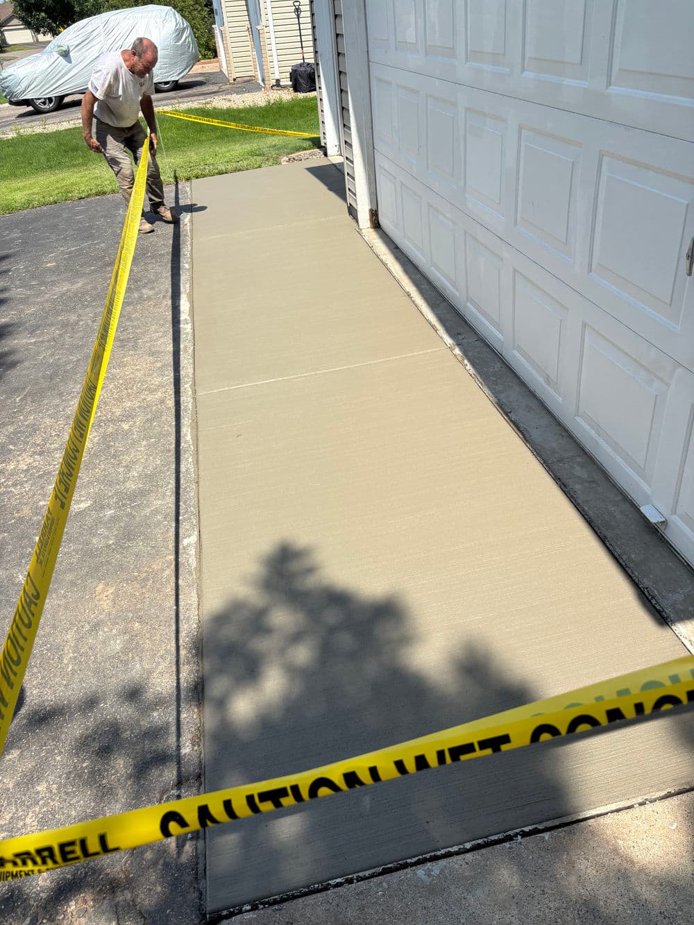 Person measuring freshly poured concrete driveway with caution tape in front of garage.