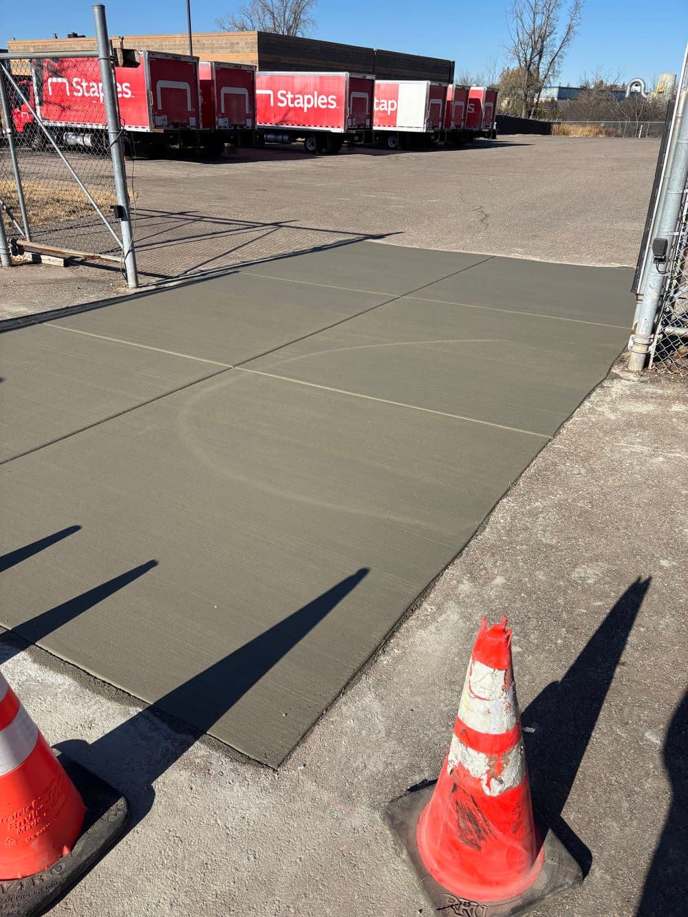 Freshly poured concrete sidewalk with traffic cones in front of a Staples distribution center.