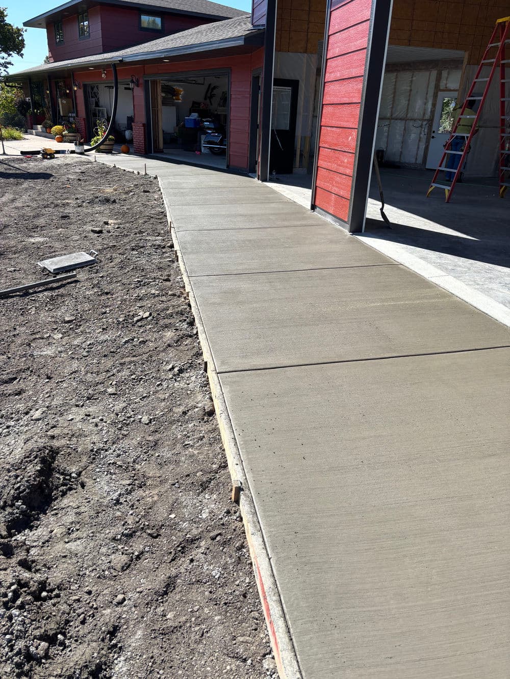 Newly poured concrete sidewalk leading to a residential garage, surrounded by gravel and landscaping.