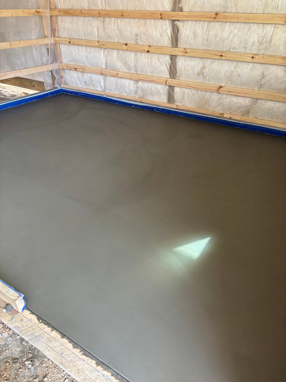 Freshly poured concrete slab in a construction enclosure with wooden framing.
