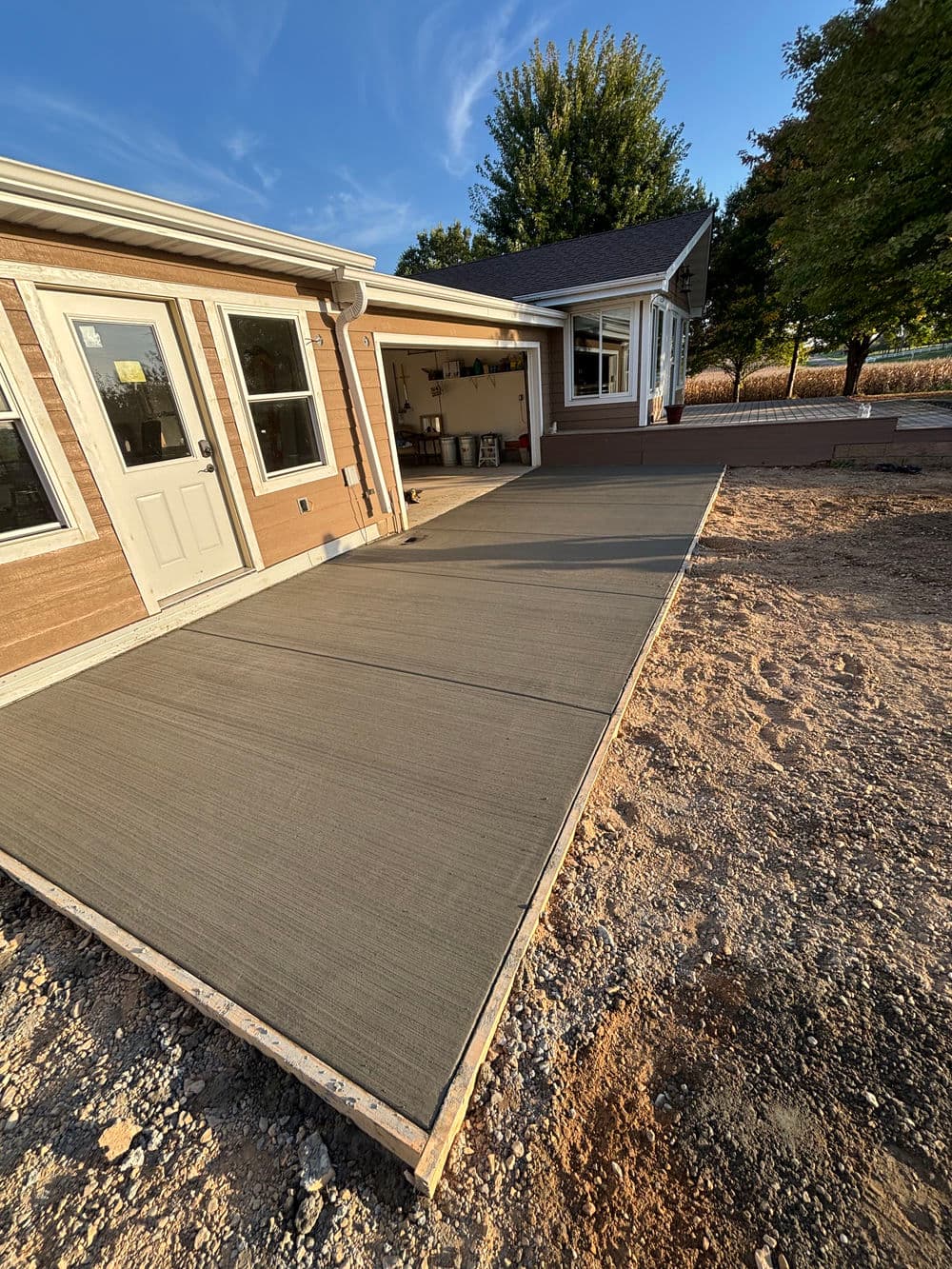 Newly poured concrete driveway beside a house with a garage on a sunny day.