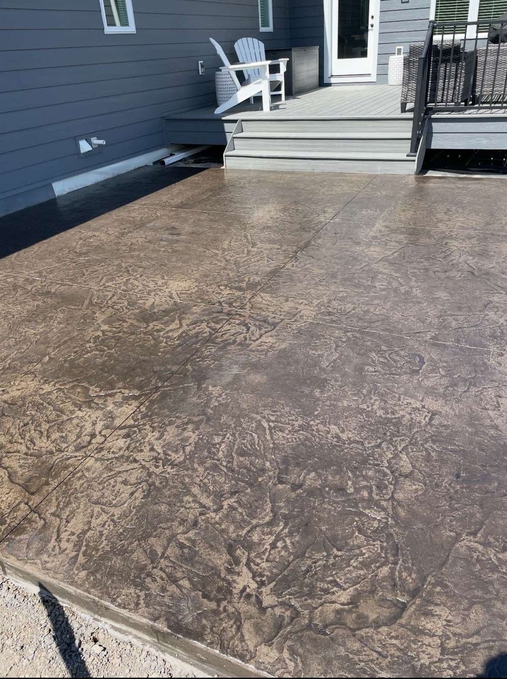 Textured decorative concrete patio with gray tones and a wooden deck in the background.