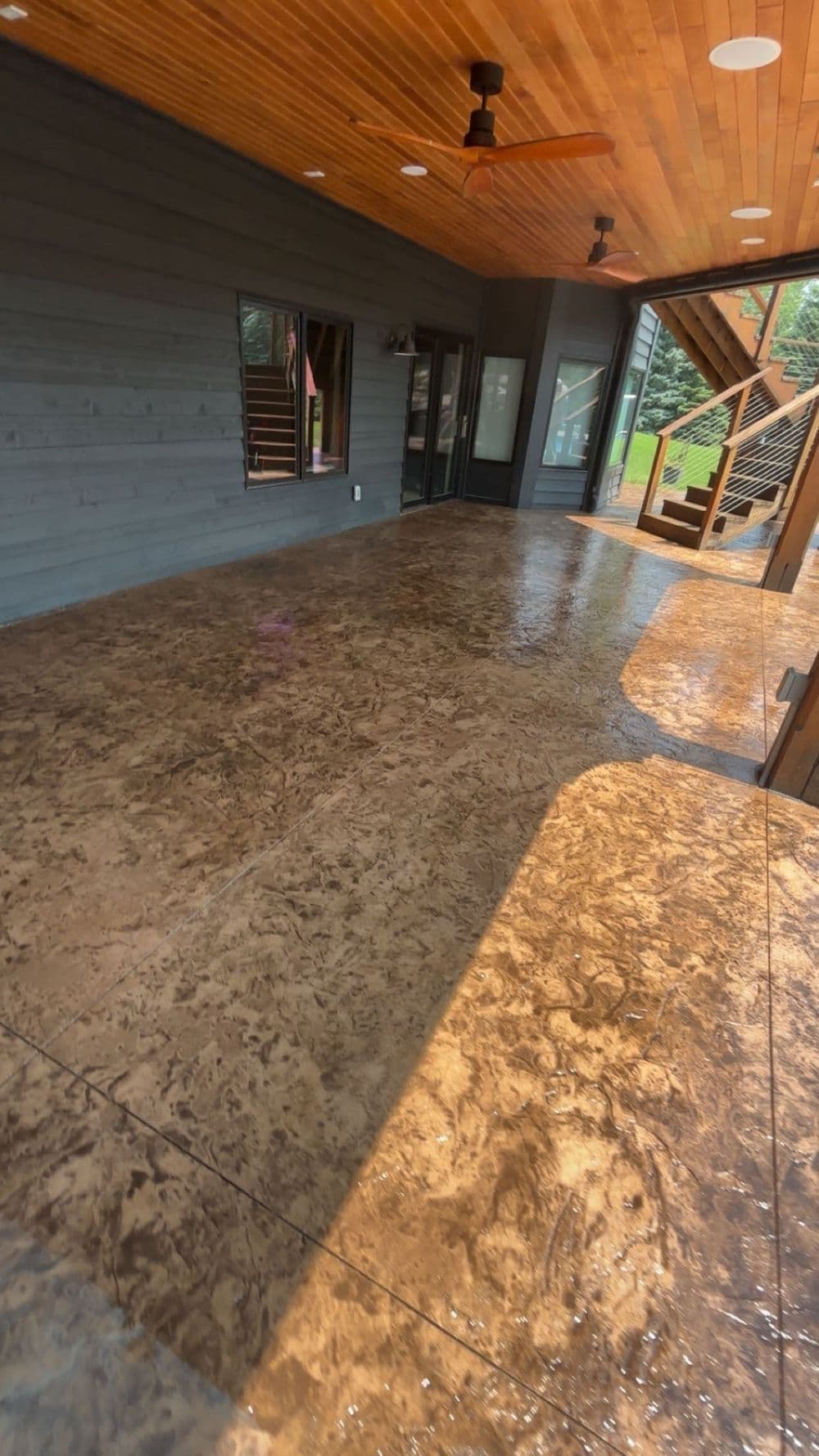 Spacious outdoor patio with polished concrete floor, wooden ceiling, and modern staircase.
