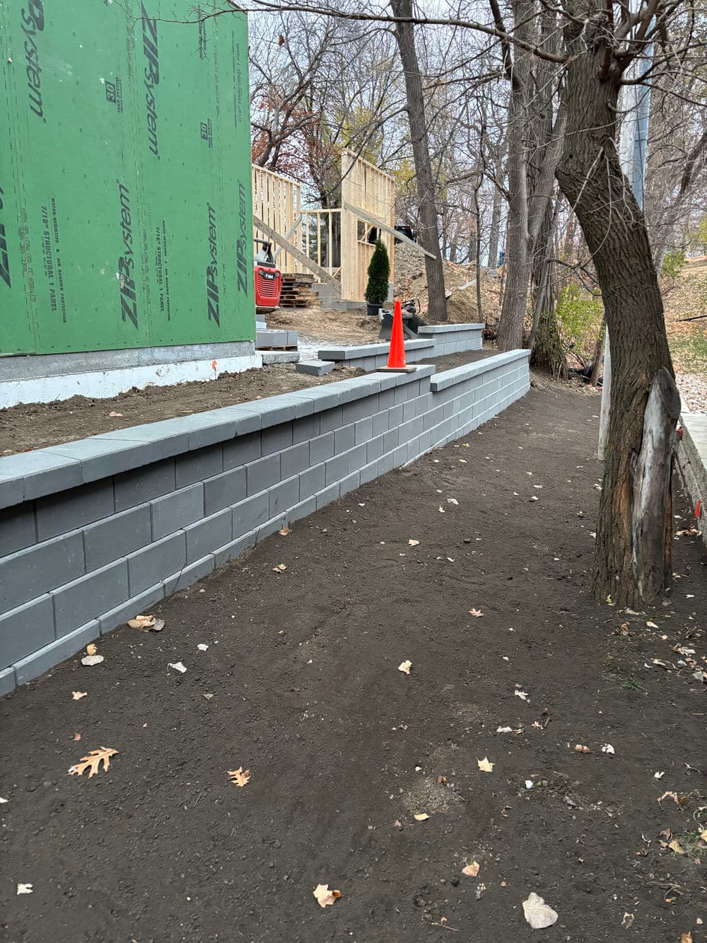 Retaining wall construction with gray blocks and orange cone near a building site.
