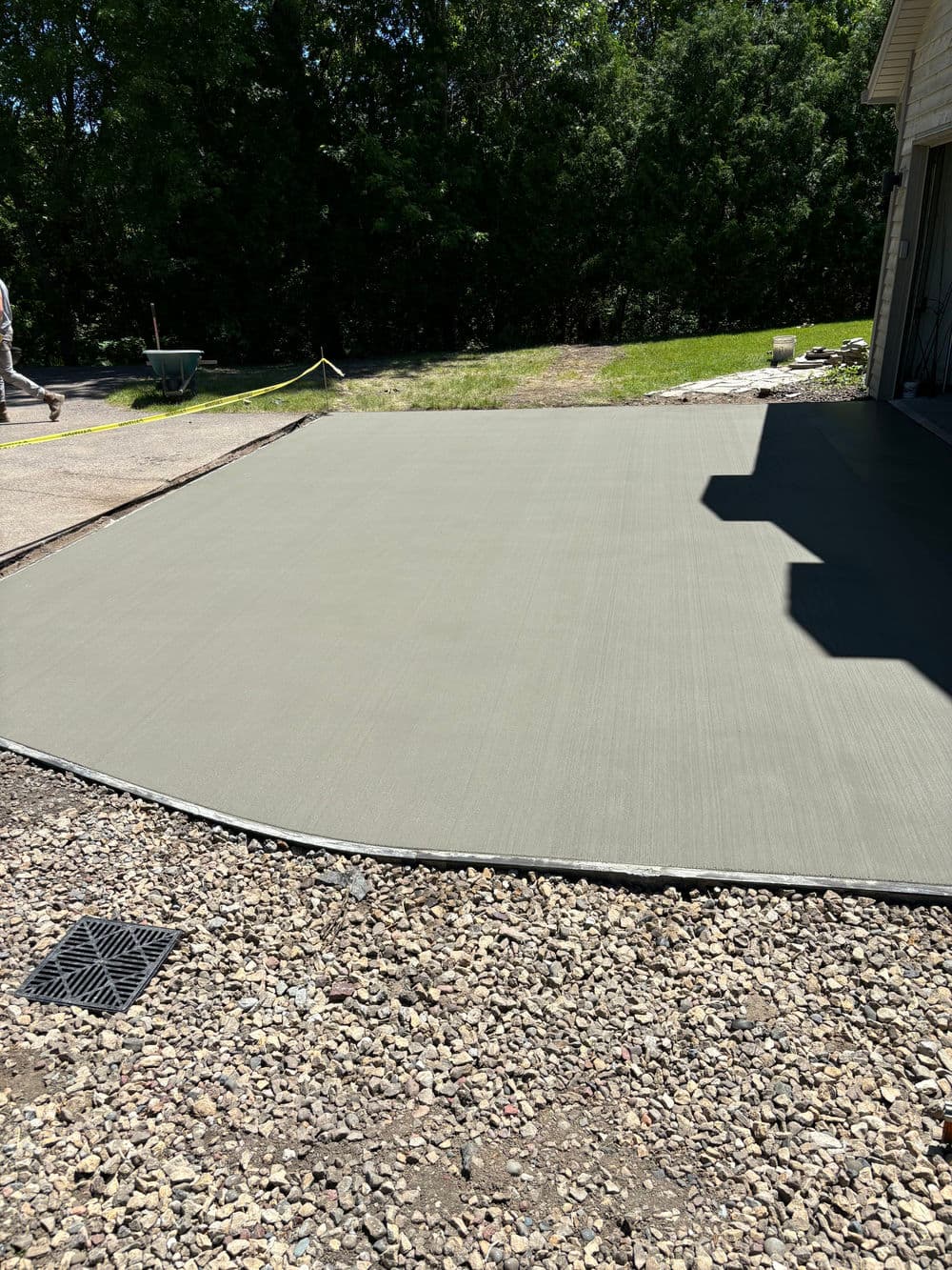 Freshly poured concrete slab in a residential yard, surrounded by a gravel border and greenery.