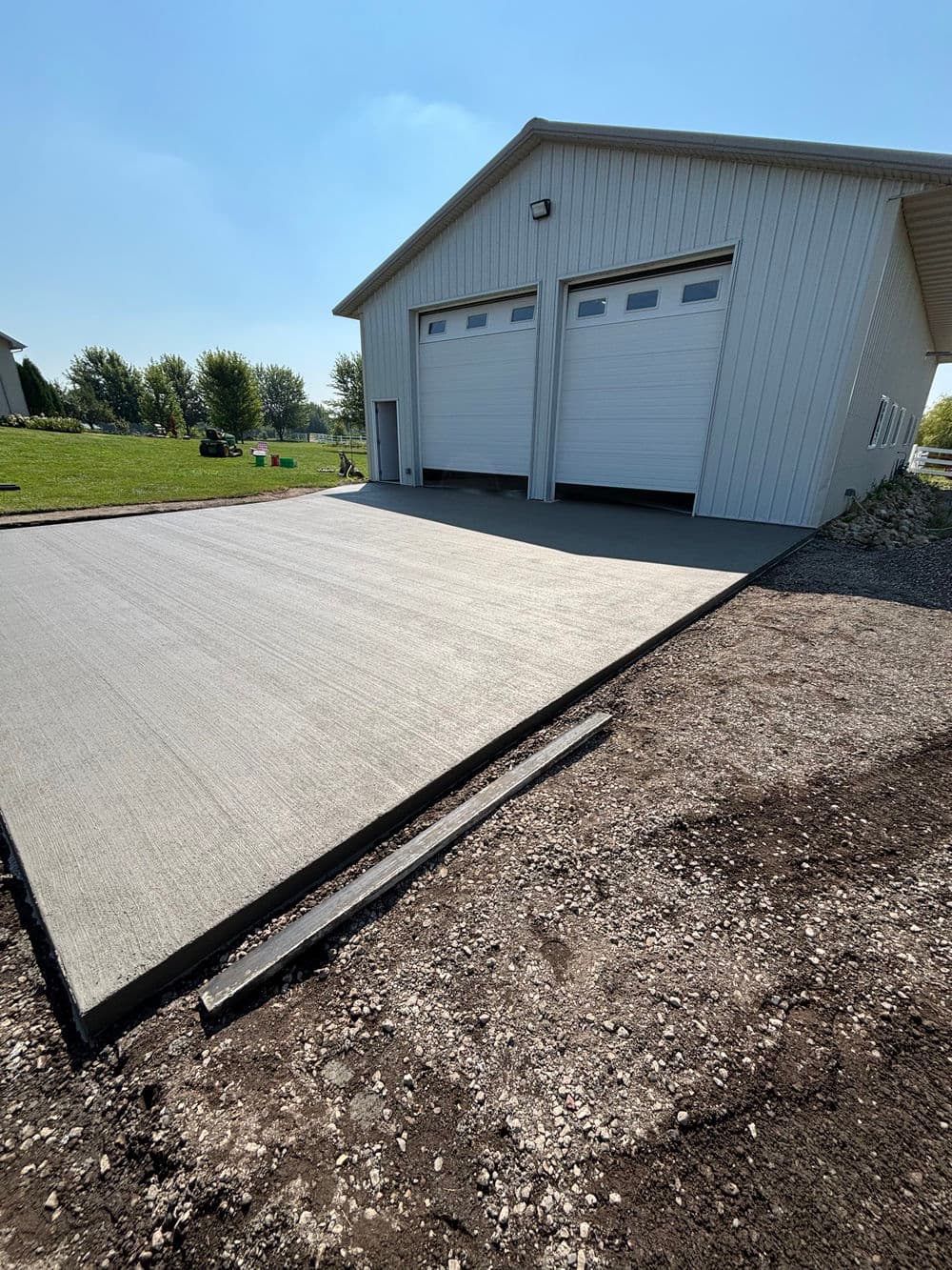 Newly poured concrete driveway beside a modern metal garage with two large doors.