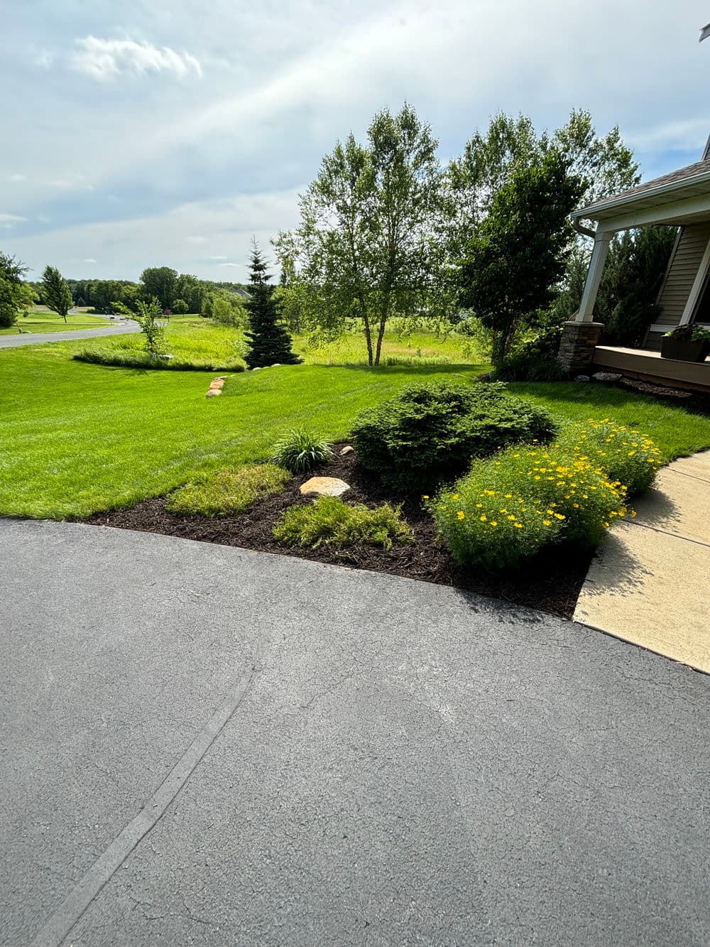 Lush green lawn with landscaped flower beds and a pathway near a house on a sunny day.