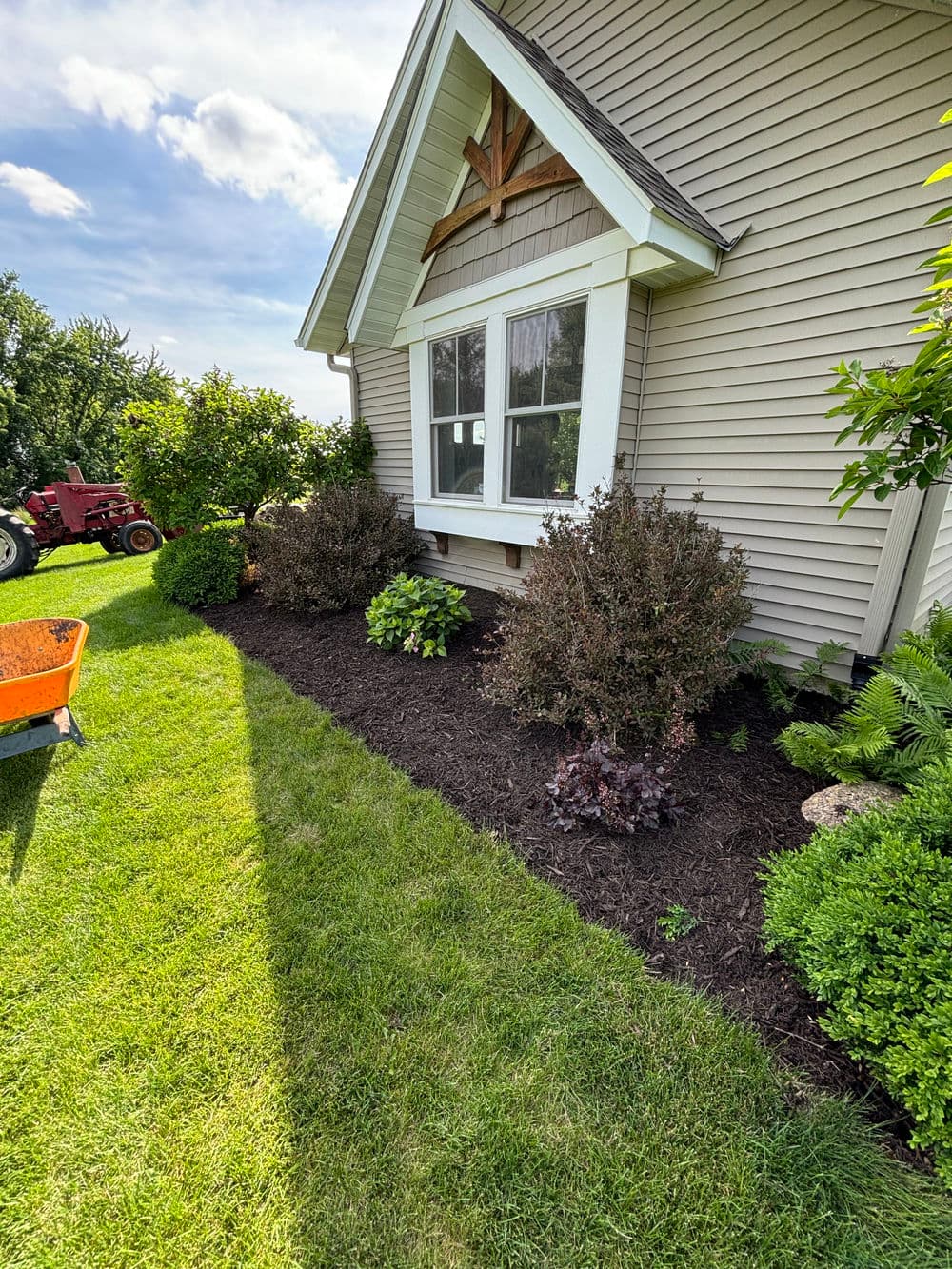 House exterior with landscaped garden and freshly mulched flower beds in bright sunlight.