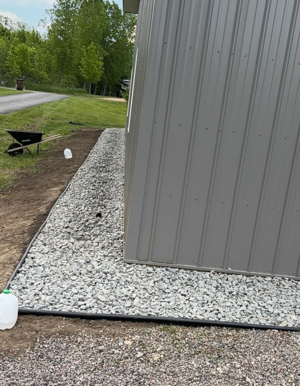 Gravel landscaping alongside a metal building with a lawn and pathway in the background.