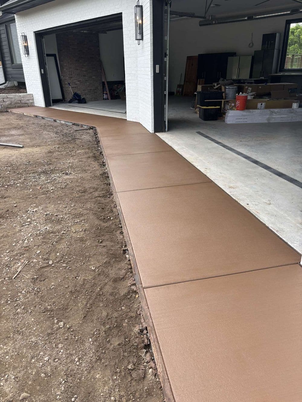 Newly poured brown concrete pathway leading to a garage, surrounded by unlandscaped soil.